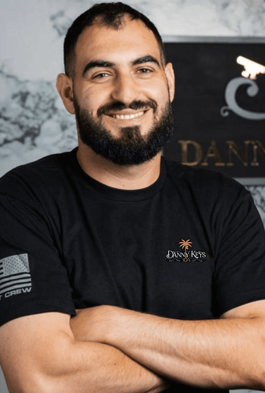 Smiling man in a black shirt with crossed arms.