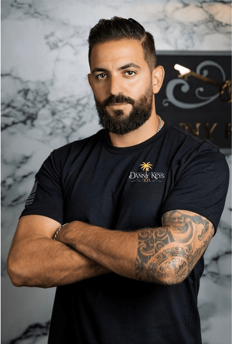Man with a beard and tattooed arms wearing a black t-shirt.