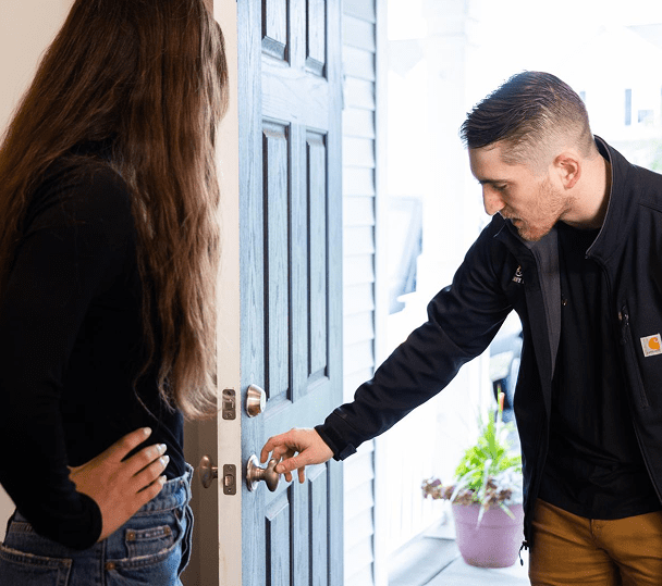 Man unlocking the front door while woman watches, ready to enter.