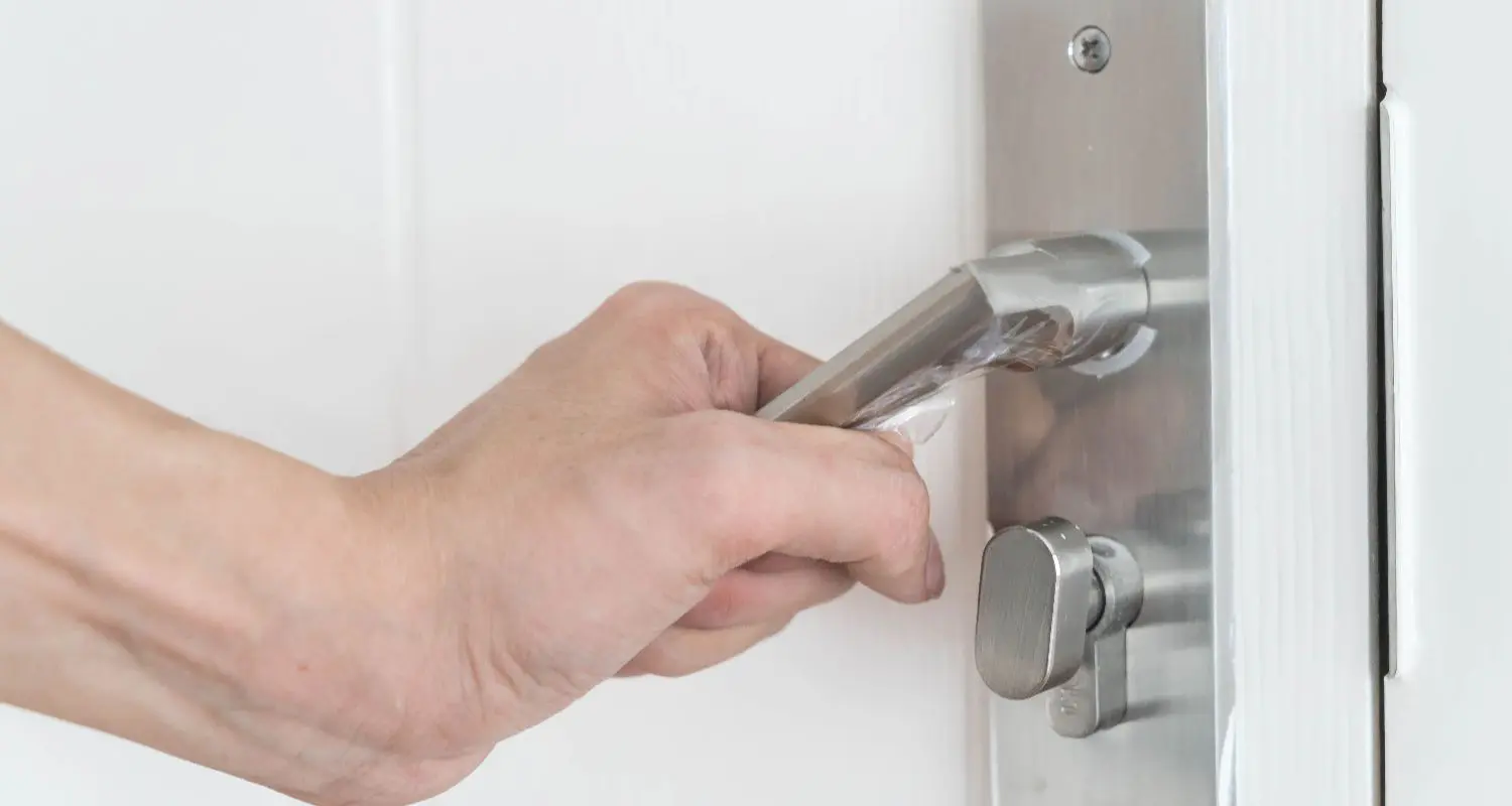 Hand gripping a metal door handle on a white door.