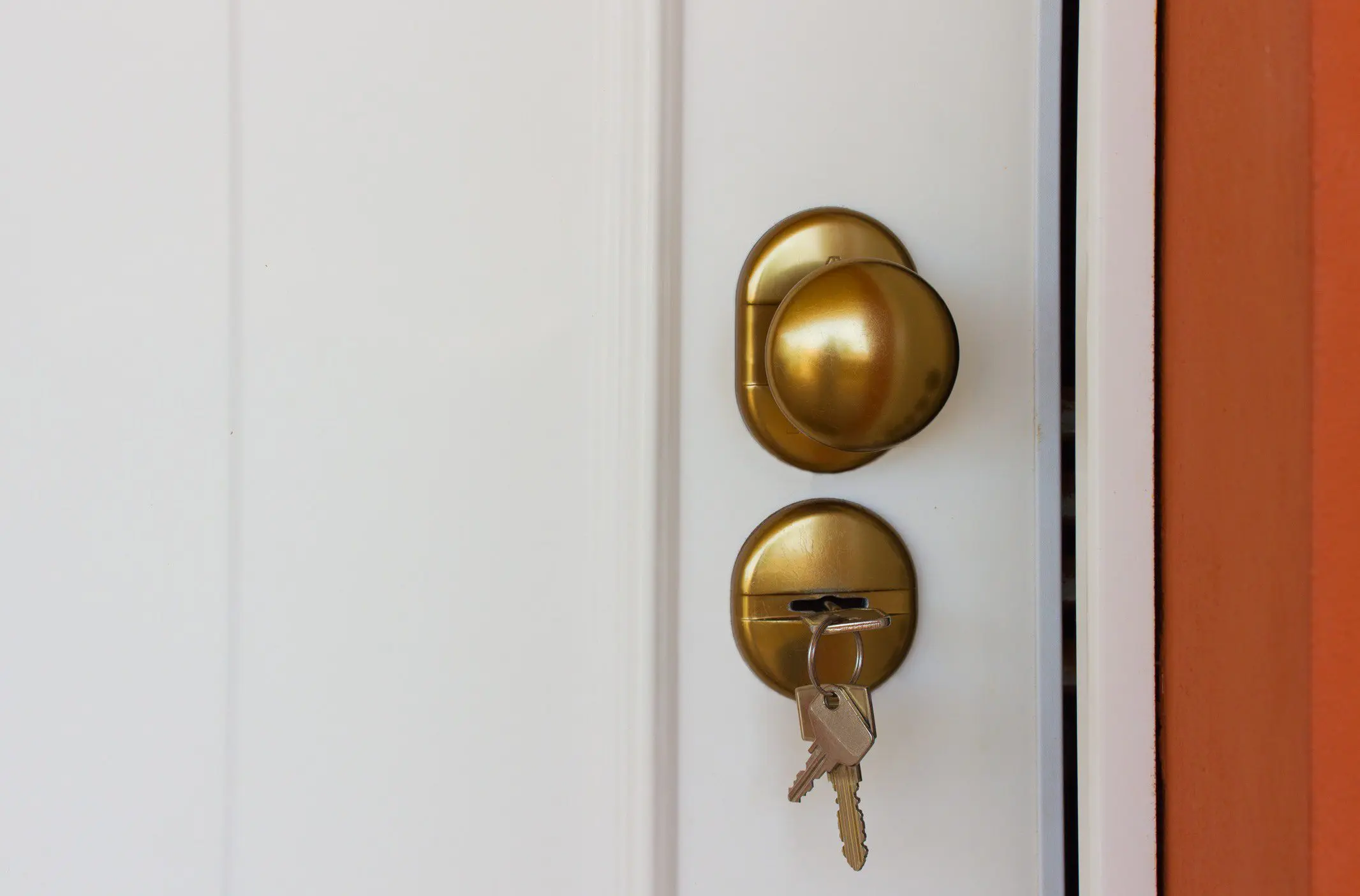 A brass doorknob and lock with keys inserted on a white door.